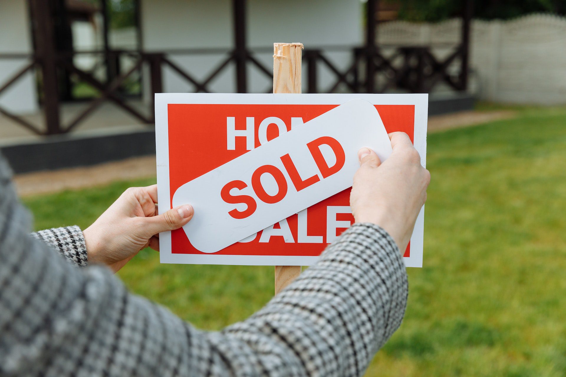 Hands placing a 'SOLD' sticker over a 'For Sale' sign in front of a residential property, symbolizing the successful real estate transactions facilitated by our company, leveraging innovative blockchain technology for secure, transparent, and efficient property management and sales.