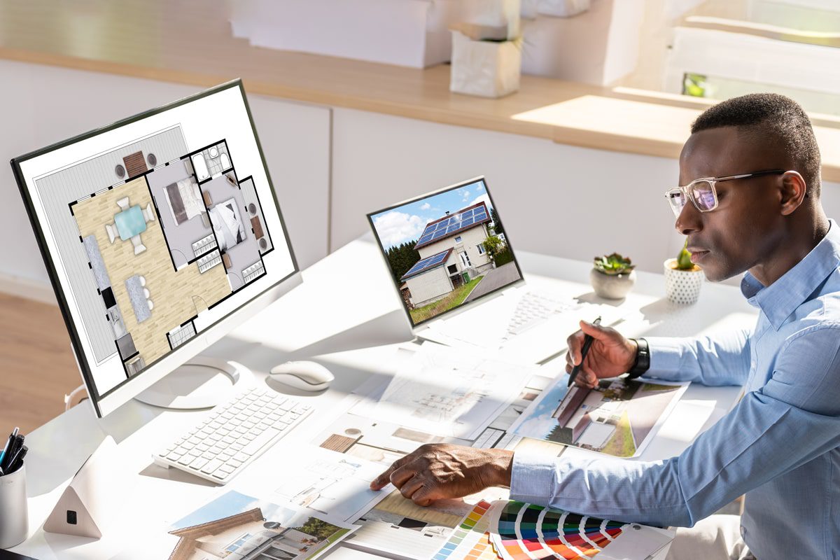 Real estate professional analyzing a 3D floor plan on a computer screen with property photos and color swatches on the desk